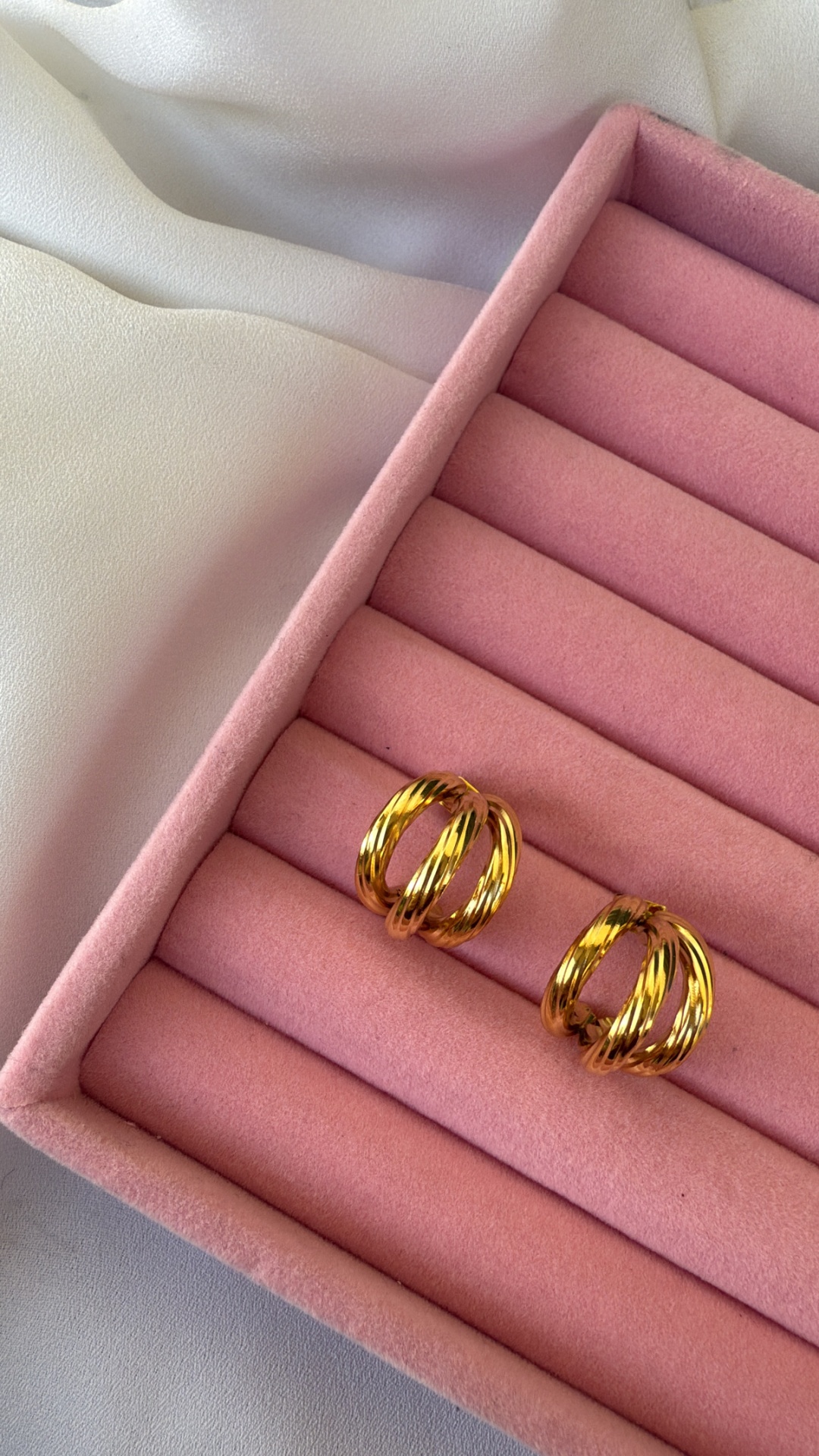 Brincos dourados em caixa de veludo rosa sobre tecido branco