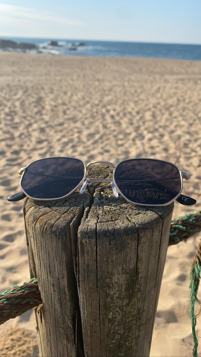 Óculos de sol de armação metal prateada sobre poste de madeira numa praia