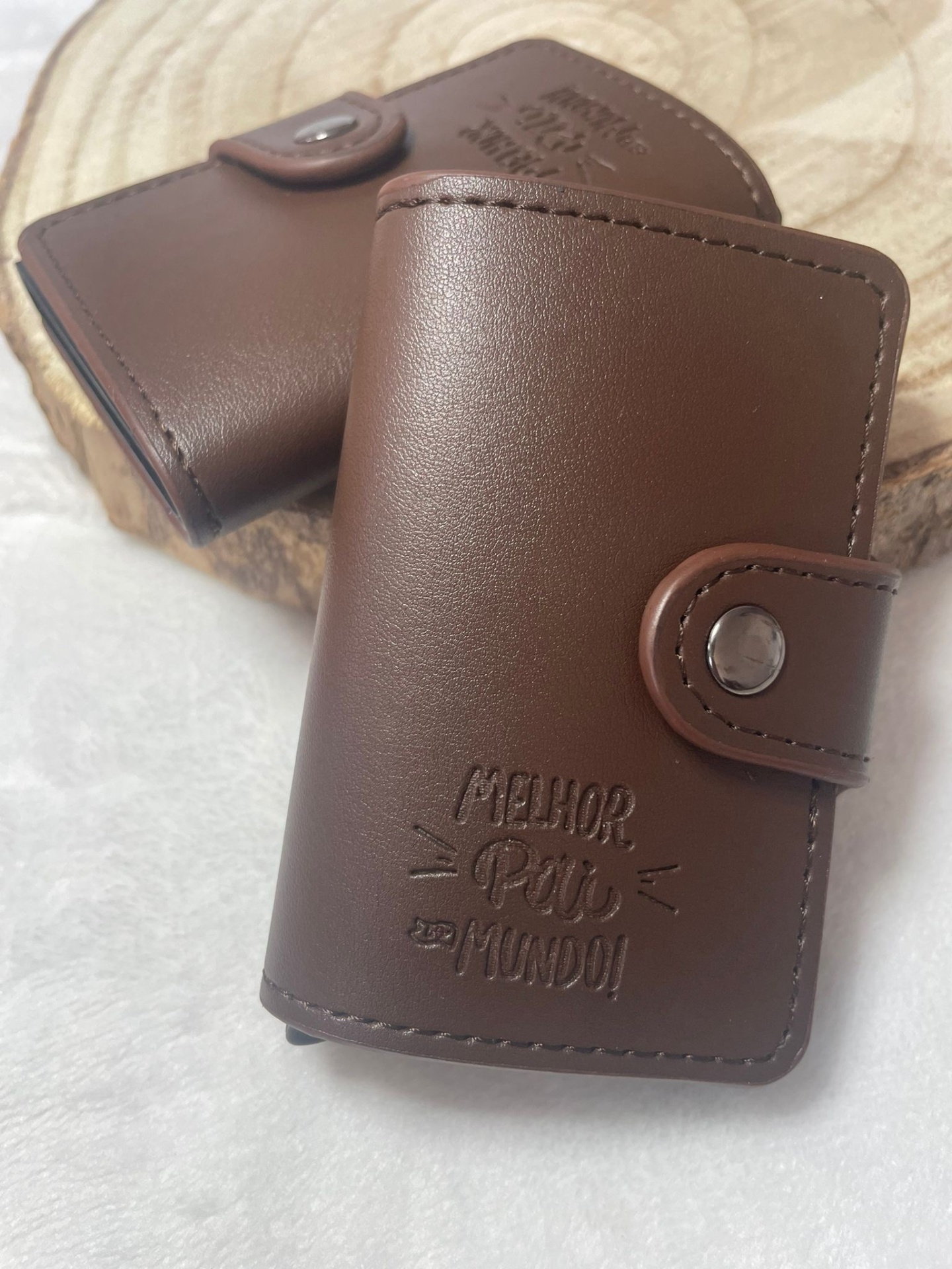 Carteiras castanhas em pele sintética com fecho metálico, uma gravada com 'MELHOR PAI DO MUNDO!'.