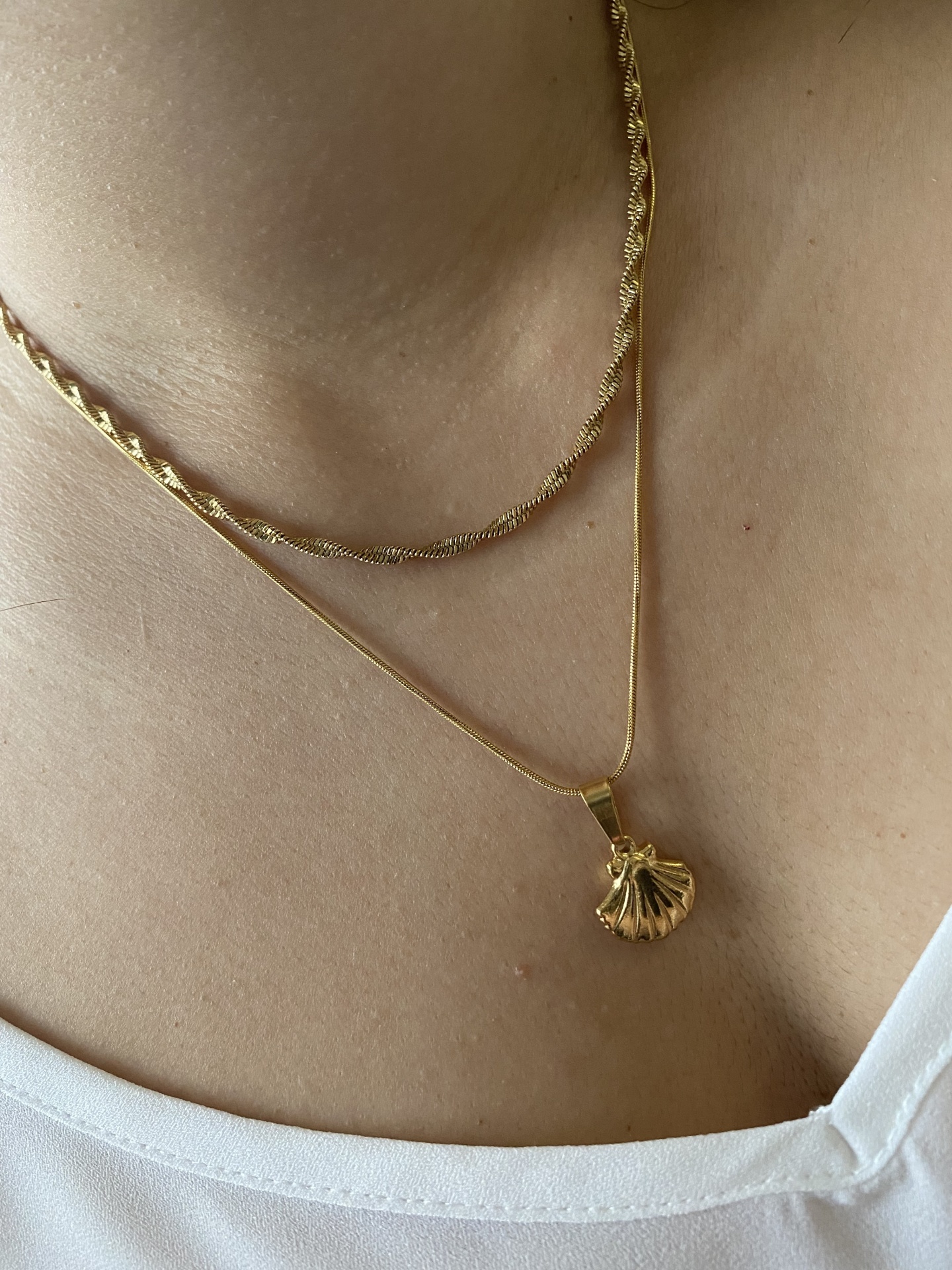Colar dourado com pendente de concha sobre pele e camiseta branca