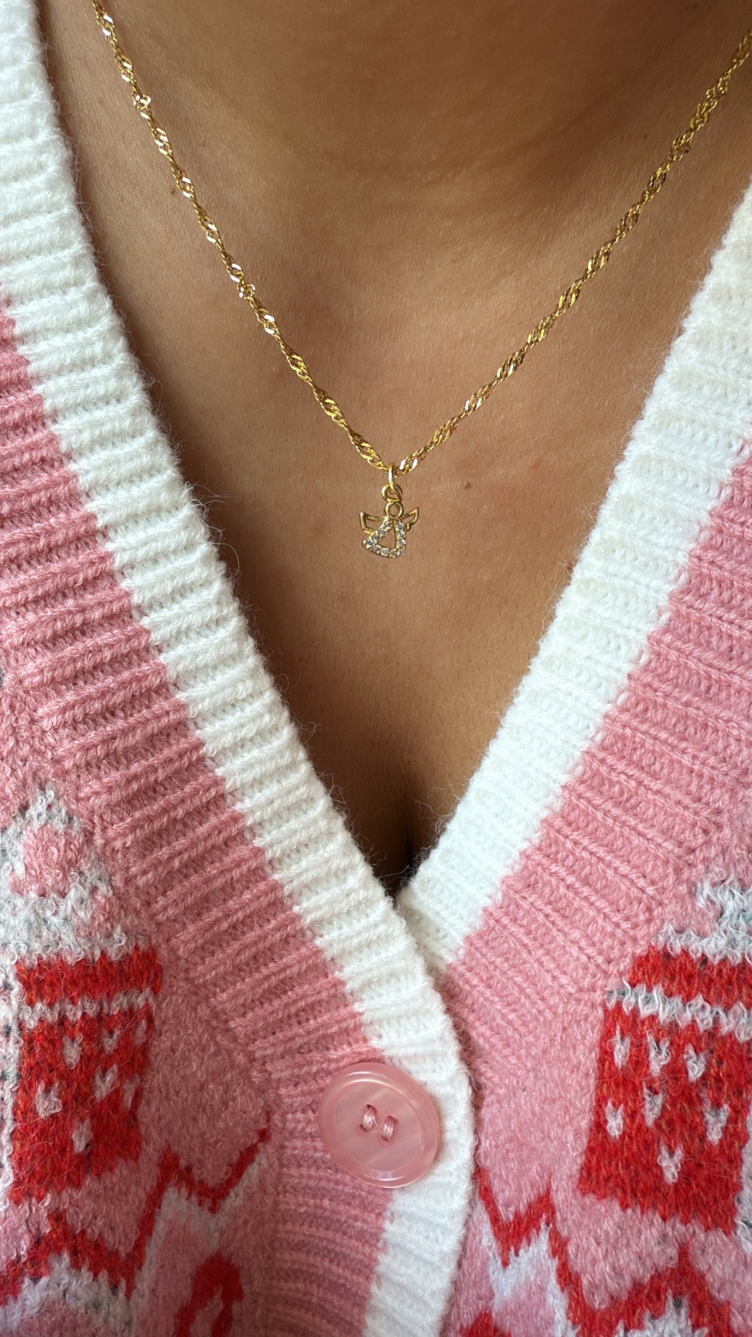 Colar dourado com pendente de anjo e camisola rosa com padrão e gola branca