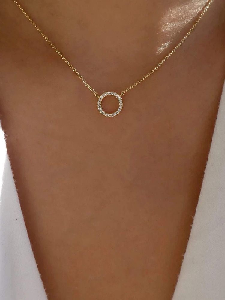 Colar dourado com pendente circular cravejado de pedras brilhantes no pescoço de uma pessoa.