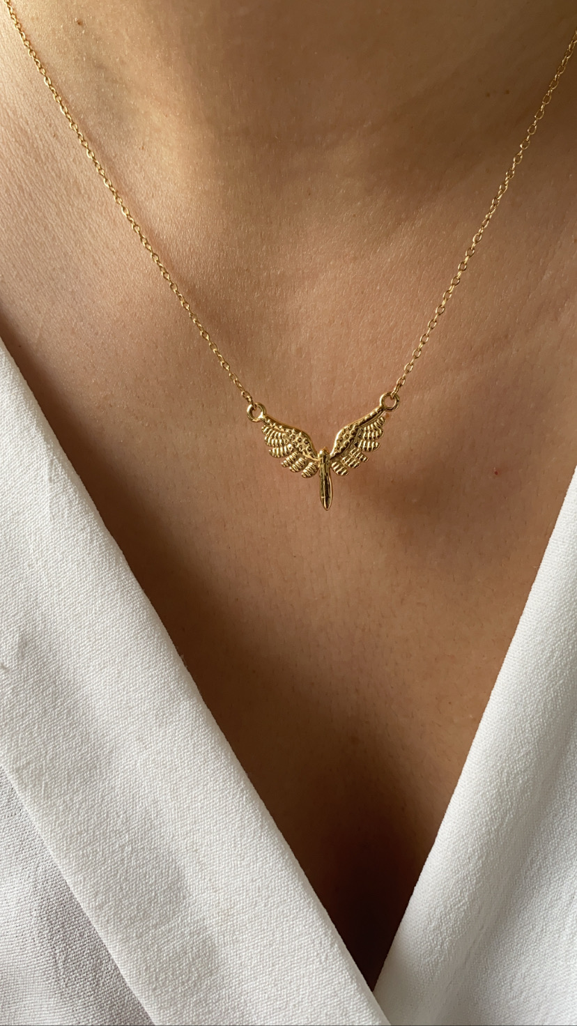Colar dourado com pendente de asas usadas sobre blusa branca