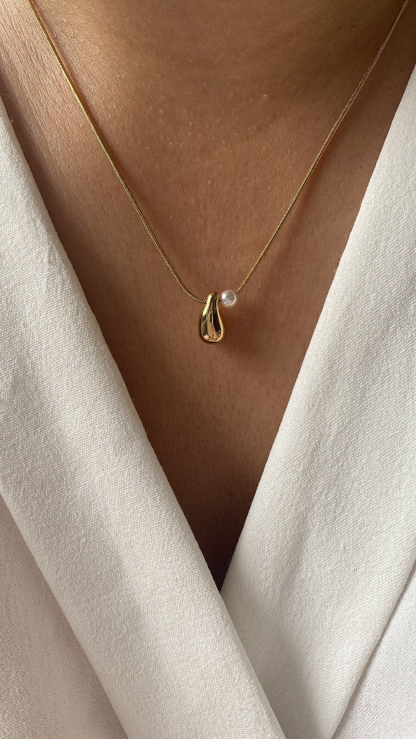 Colar dourado com pendente e pérola em pescoço, roupa branca