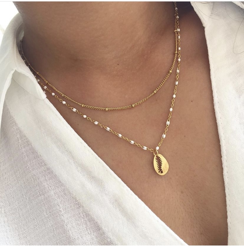 Colar duplo dourado com pérolas e medalha com desenho de folha, usado com camisa branca