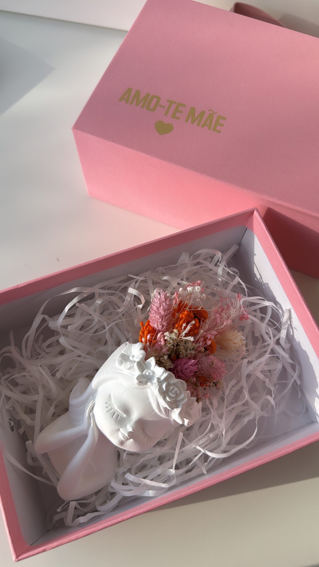 Caixa rosa com texto AMO-TE MÃE dourado e escultura branca com flores secas coloridas dentro