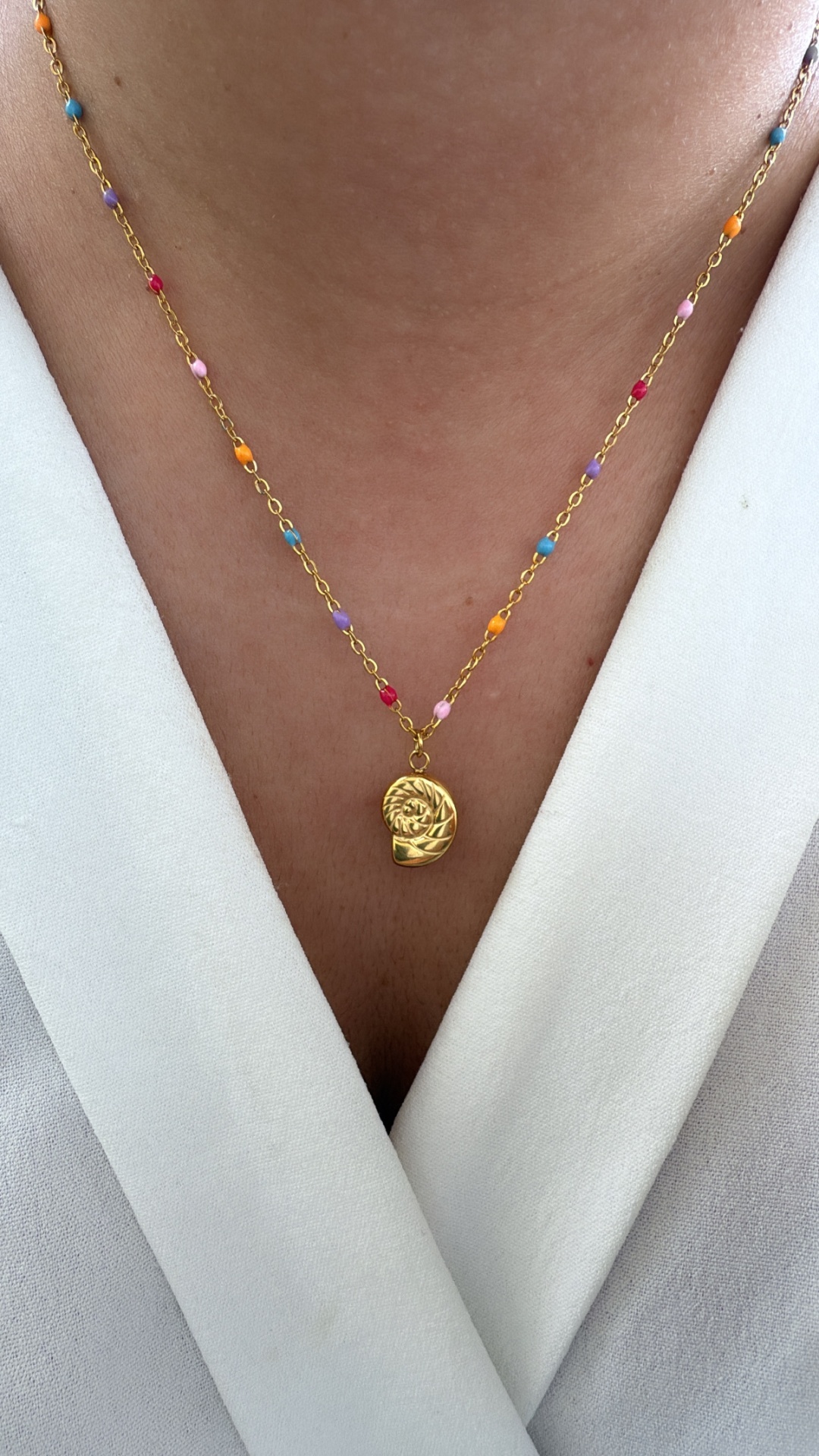 Colar dourado com contas coloridas e pendente abstrato usado sobre camisa branca