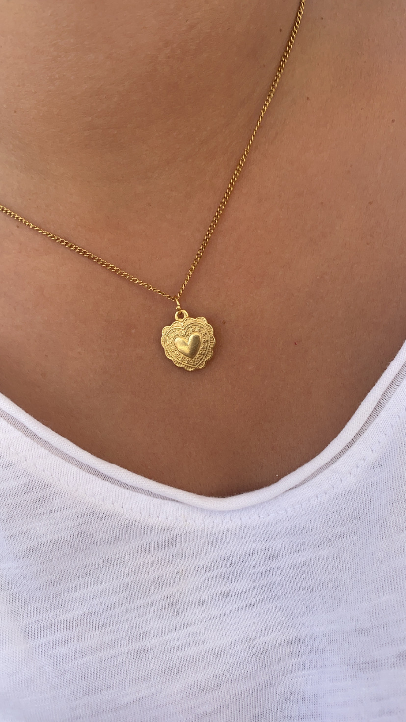 Colar dourado com pendente em forma de coração em pele e blusa branca