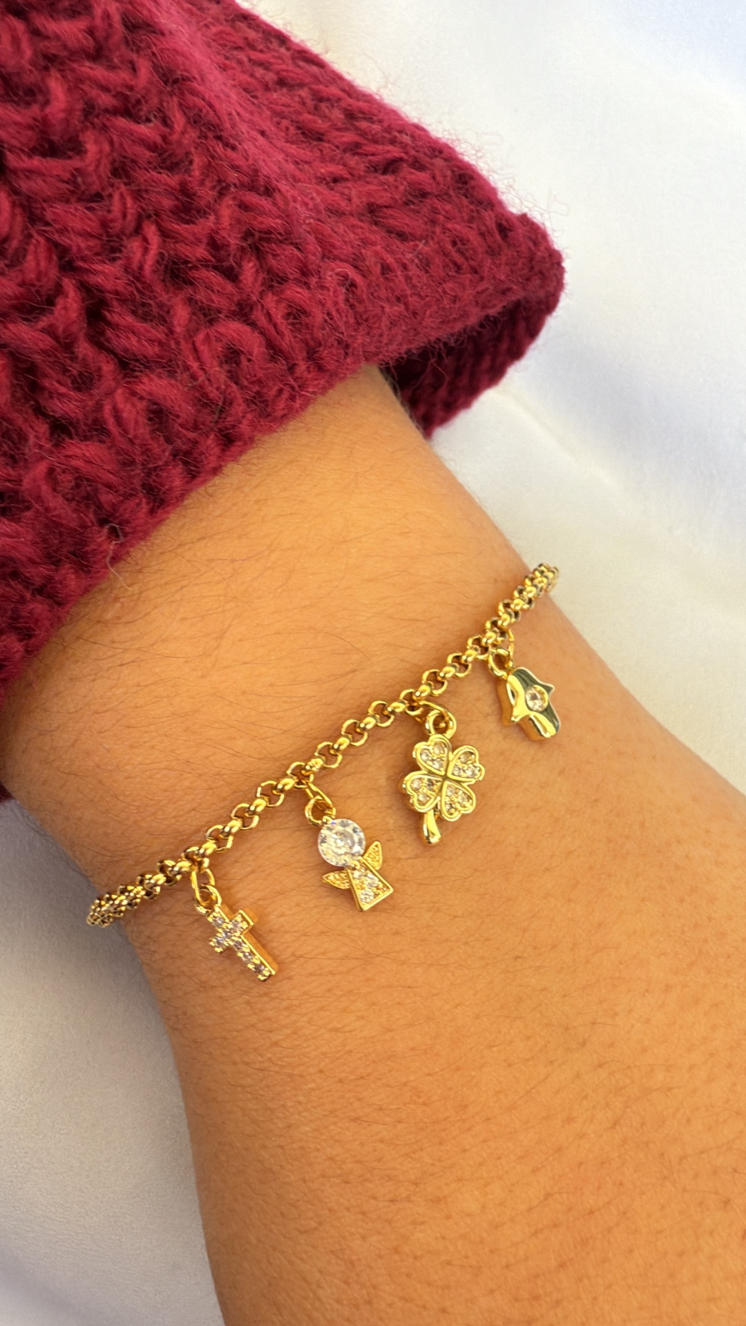 Pulseira dourada com pendentes diversos em pulso com camisola vermelha de malha