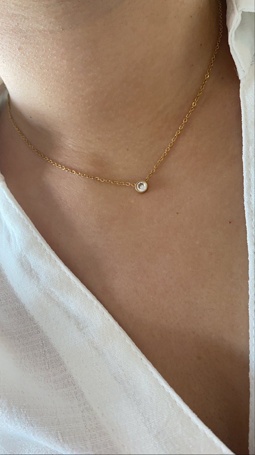 Colar dourado com pendente redondo pequeno usado no pescoço com camisa branca