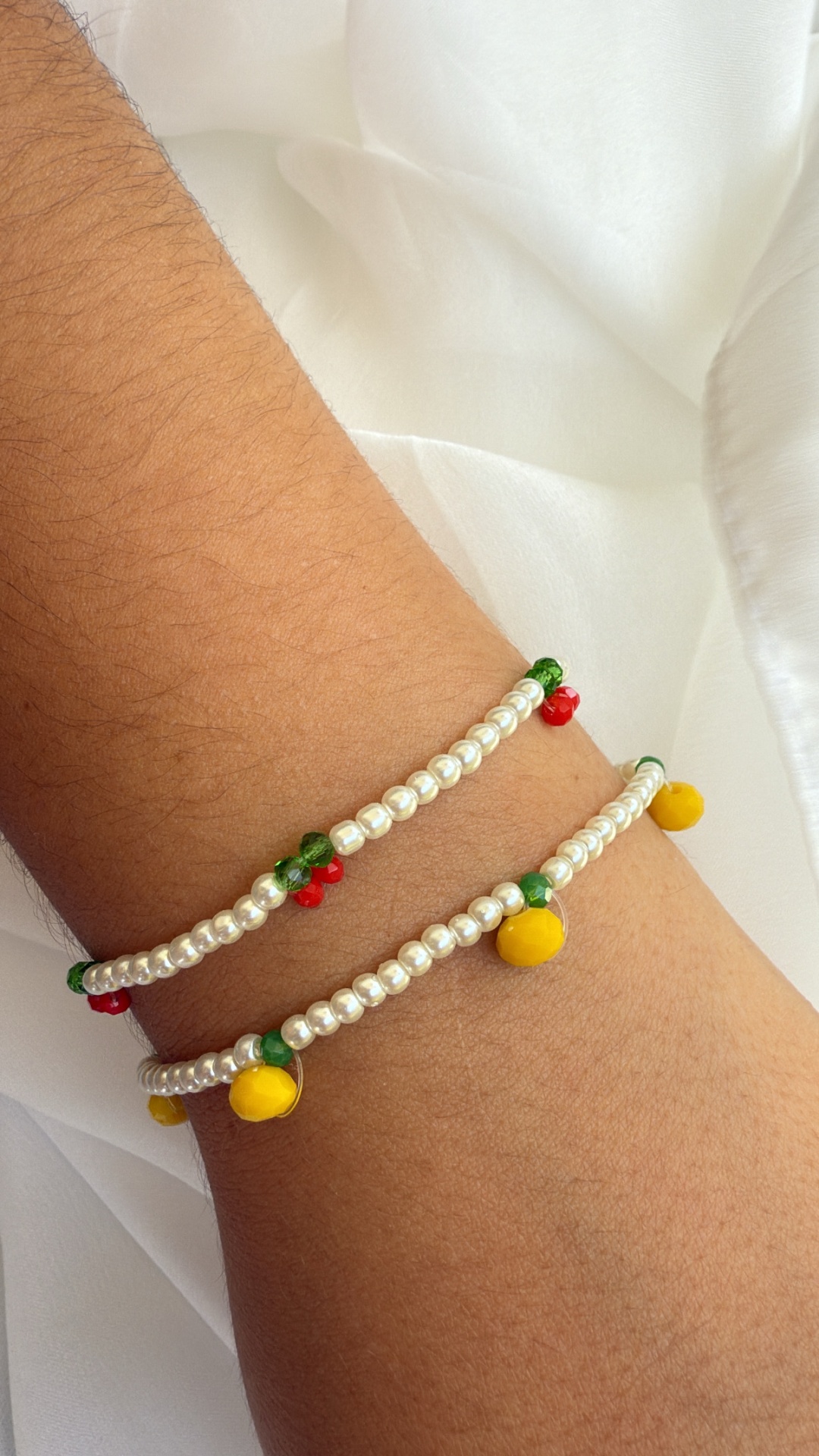 Braceletes com contas brancas e detalhes coloridos no pulso