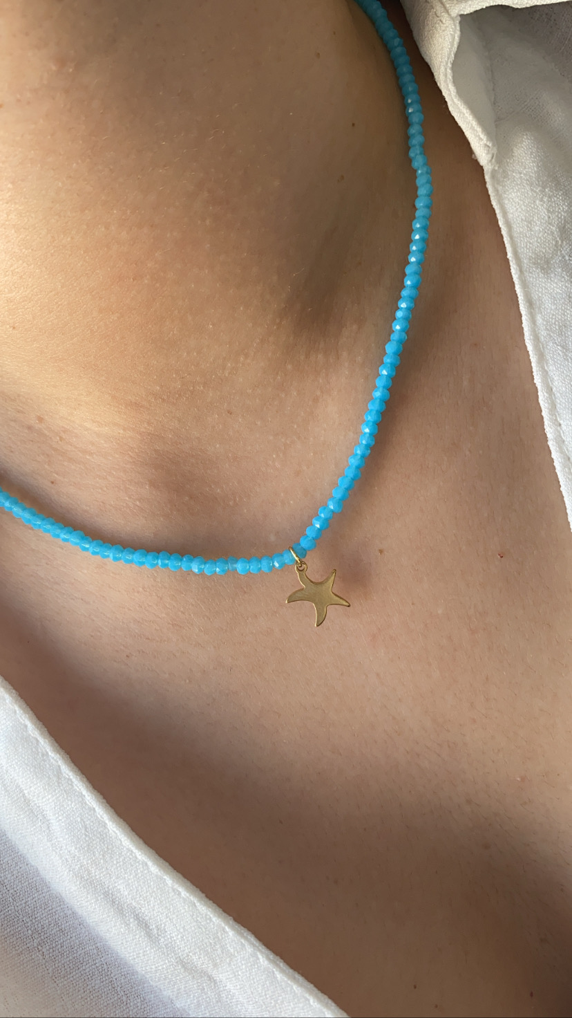 Colar azul com pendente estrela do mar dourado num pescoço.