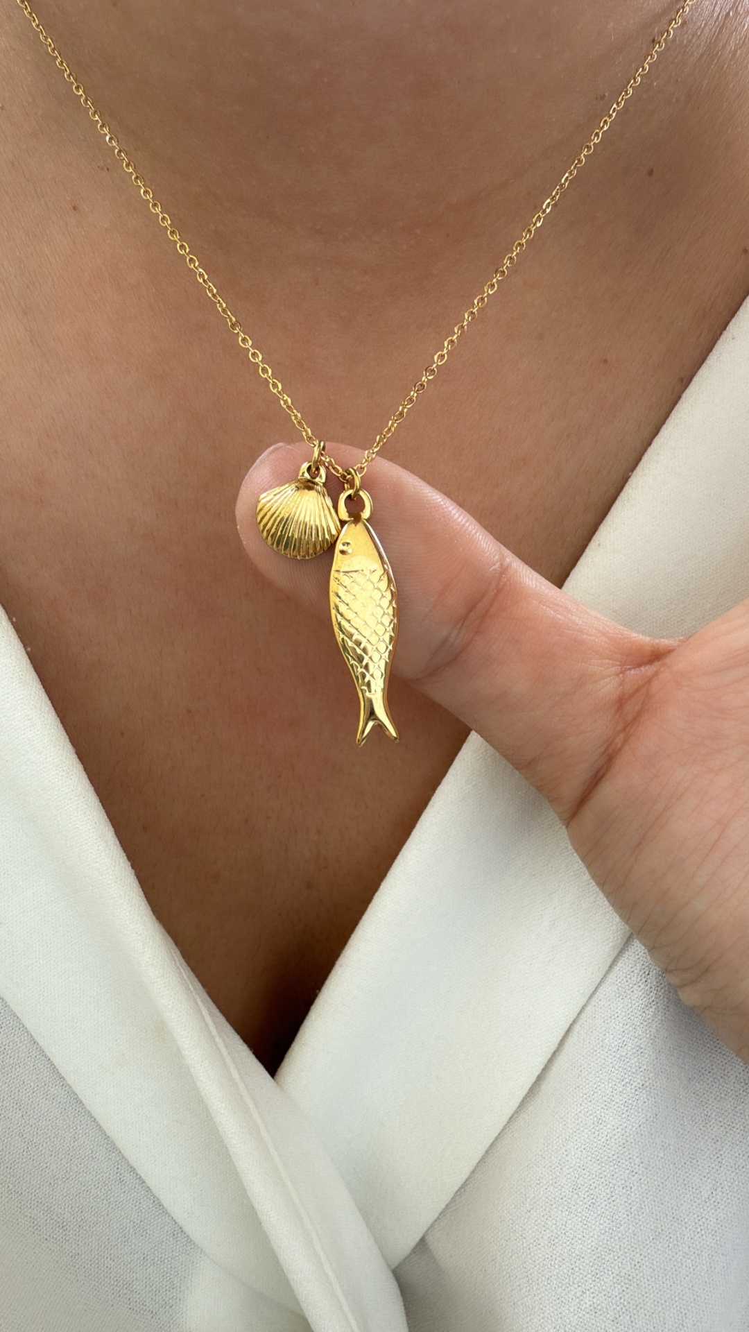 Colar dourado com pendentes de peixe e concha em roupa branca