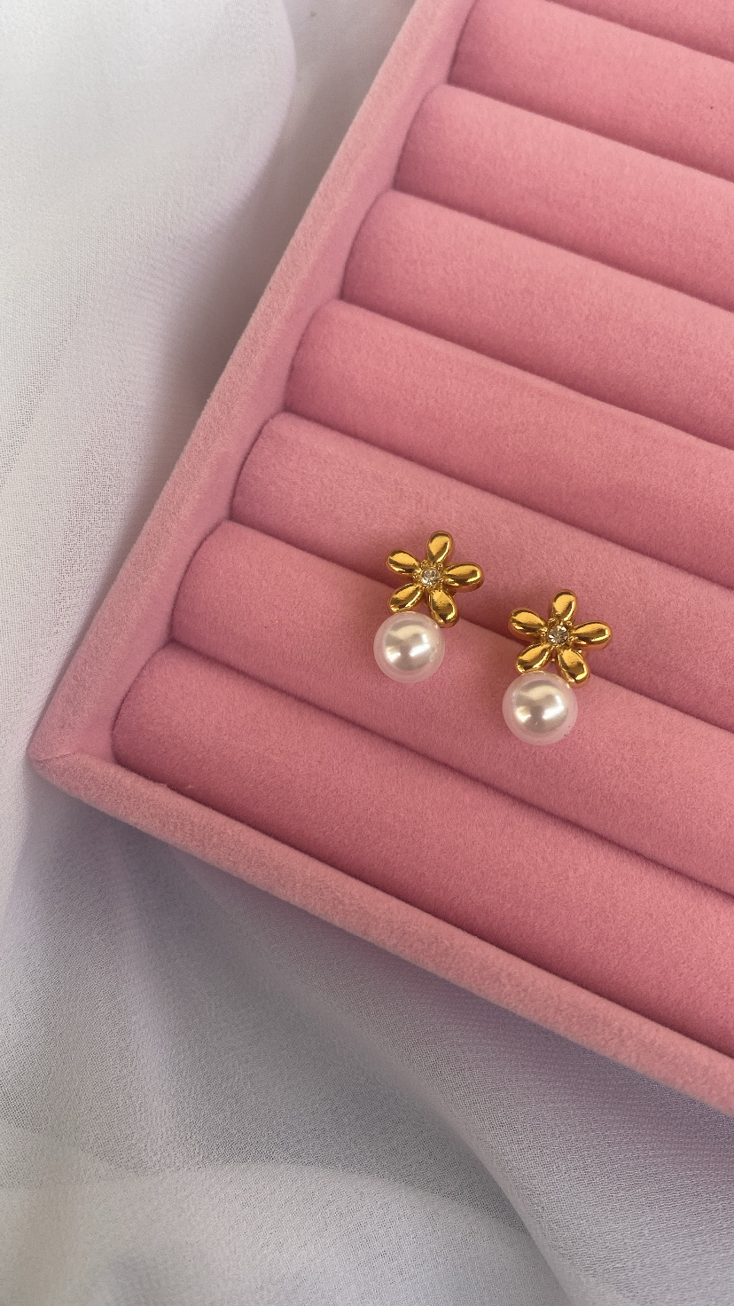 Brincos dourados em forma de flor com pérola numa caixa de veludo rosa