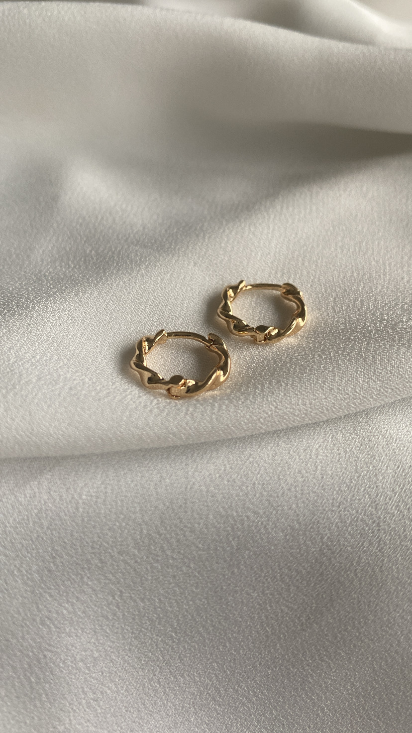 Brincos de argola dourados com design torcido sobre tecido branco.