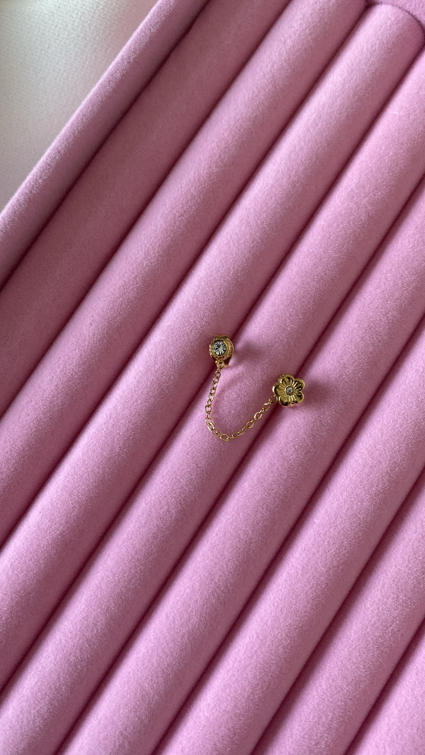 Brinco dourado com corrente e decoração floral sobre veludo rosa acolchoado