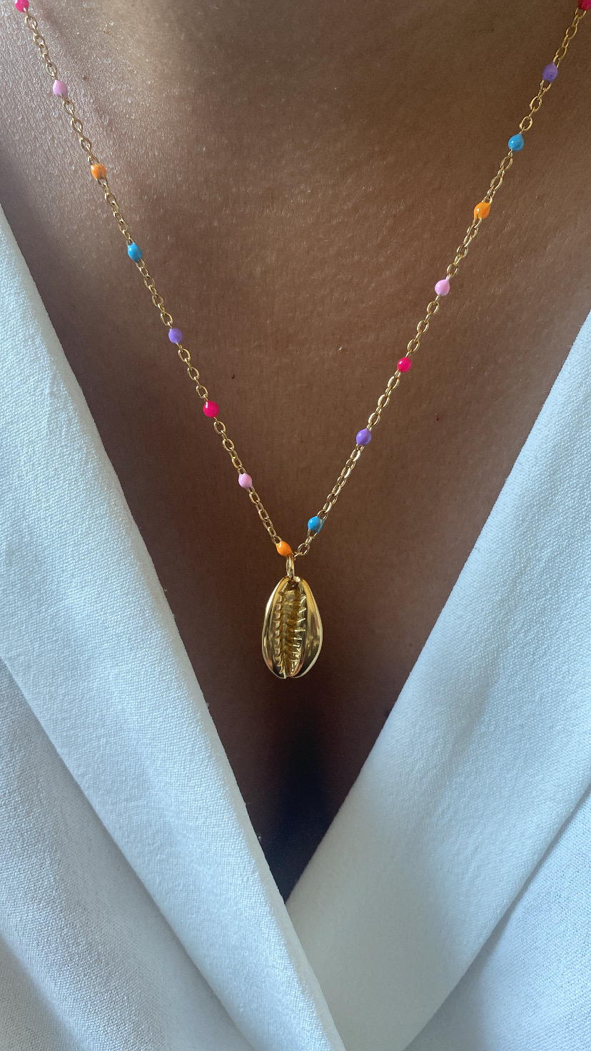 Colar dourado com contas coloridas e pendente concha sobre pele e roupa branca