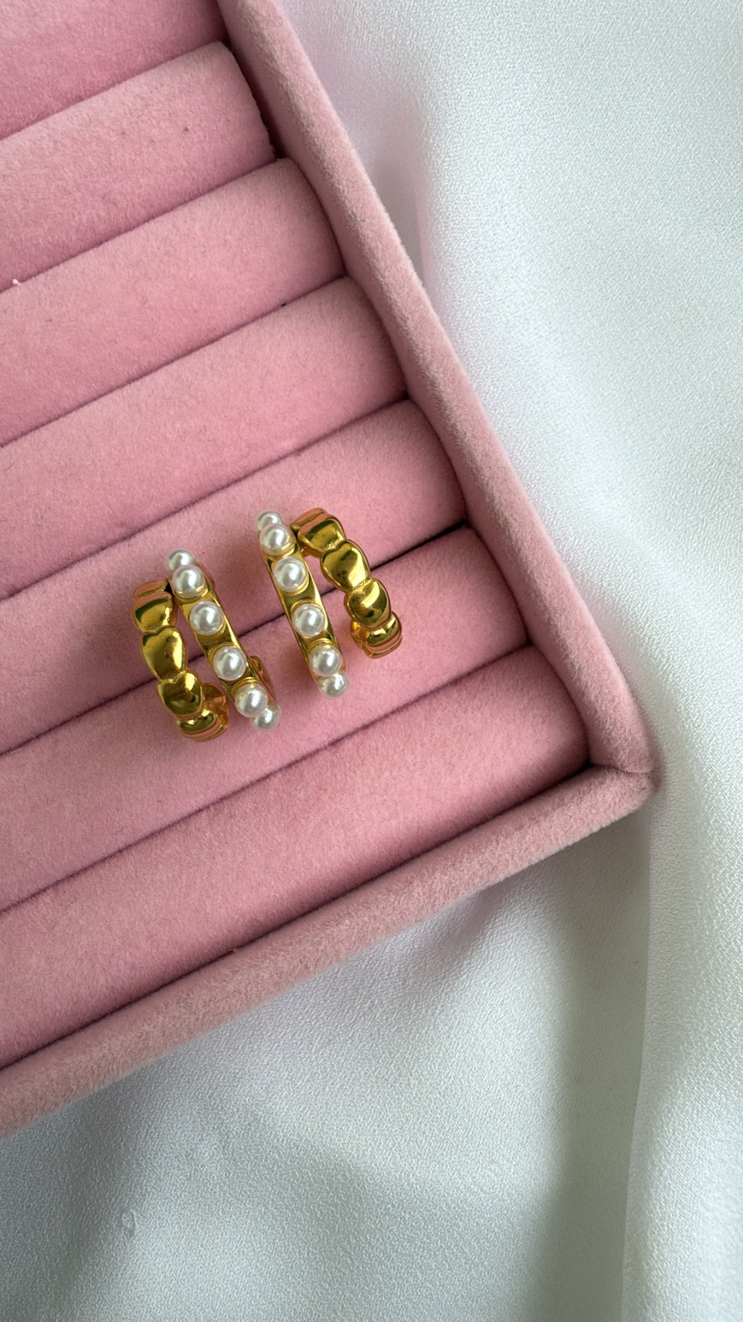 Brincos dourados com pérolas numa caixa rosa de veludo