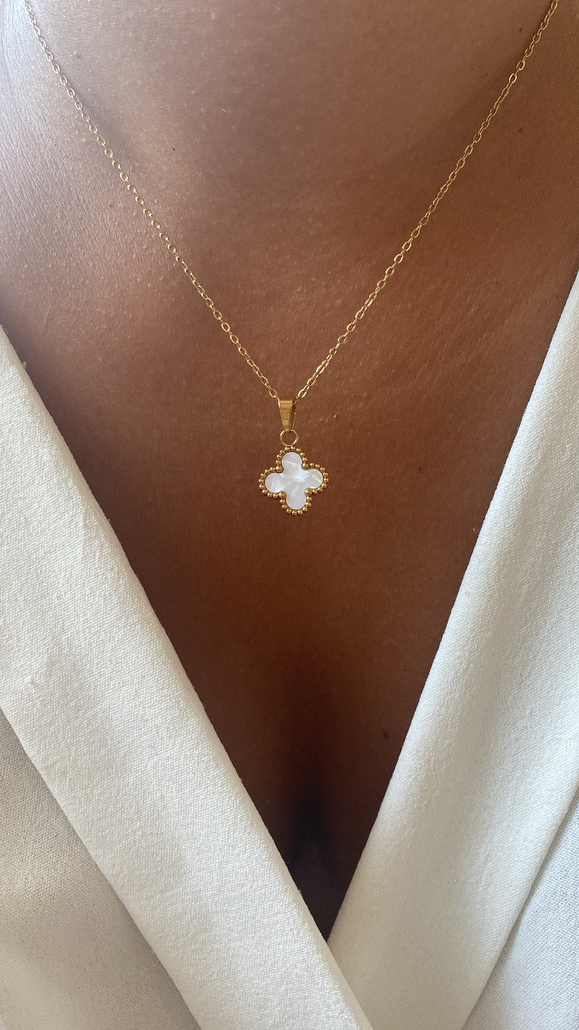 Colar dourado com pendente em forma de trevo e parede branca