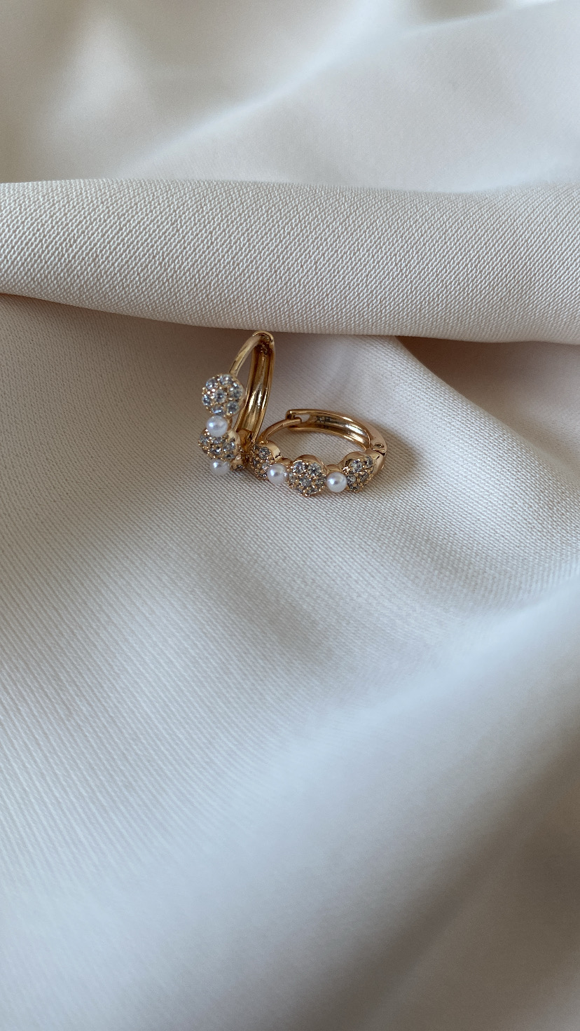 Brincos dourados com pérolas e pedras brilhantes sobre tecido branco