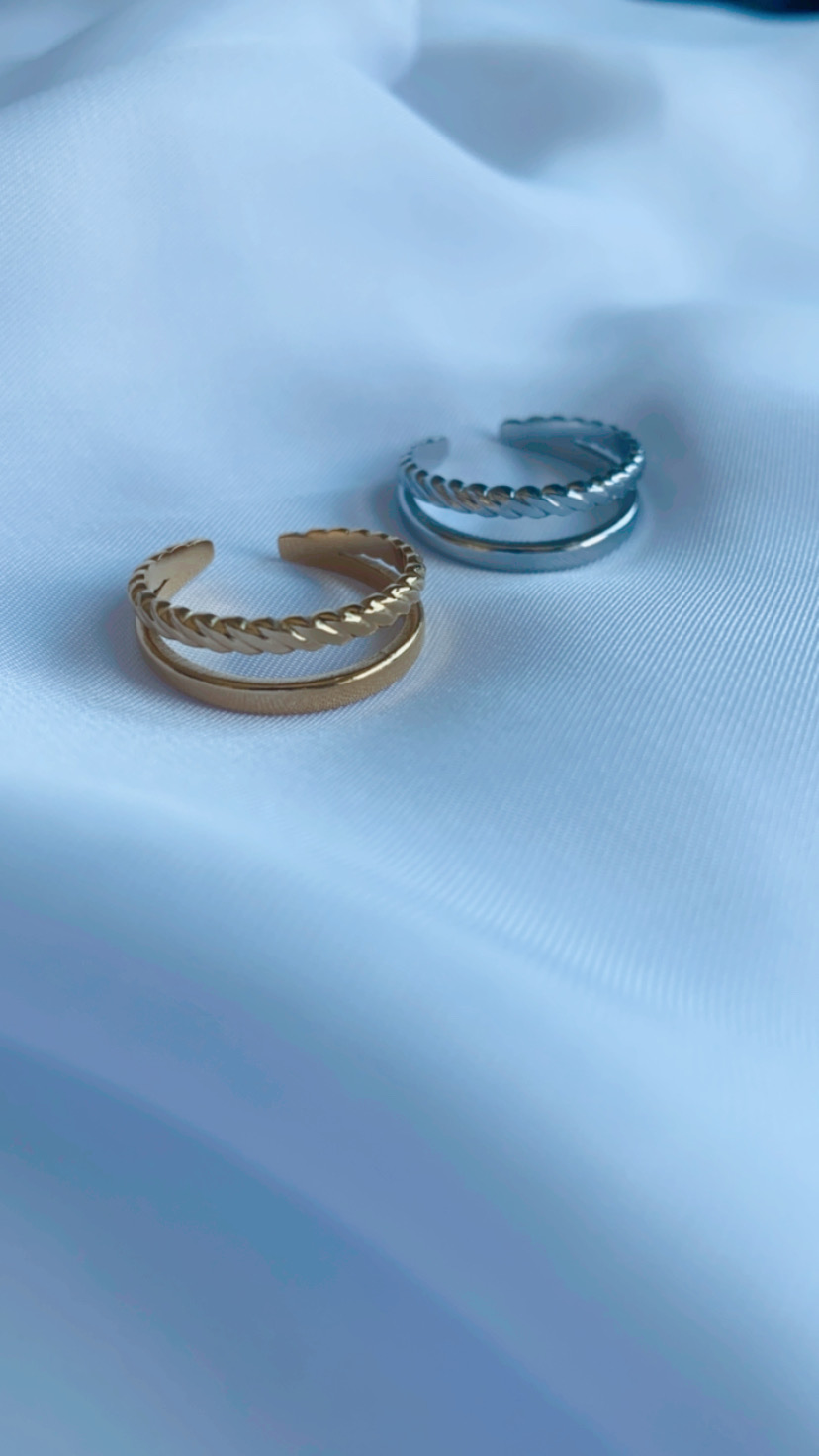 Dois anéis metálicos, dourado e prateado, sobre tecido branco