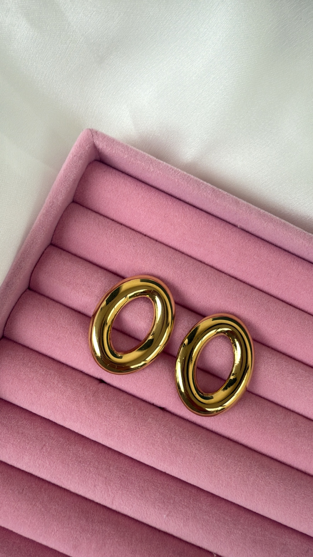Par de brincos ovais dourados em caixa rosa de veludo
