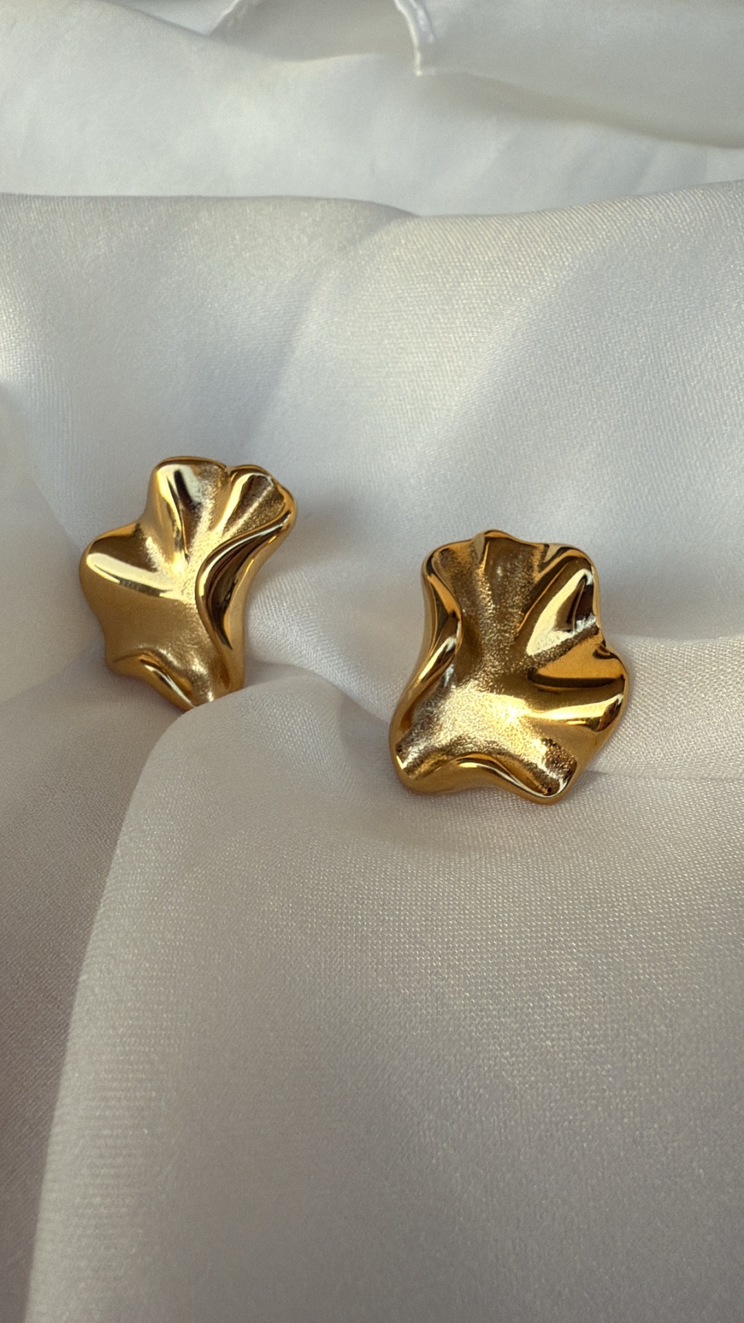 Brincos dourados com forma irregular sobre tecido branco