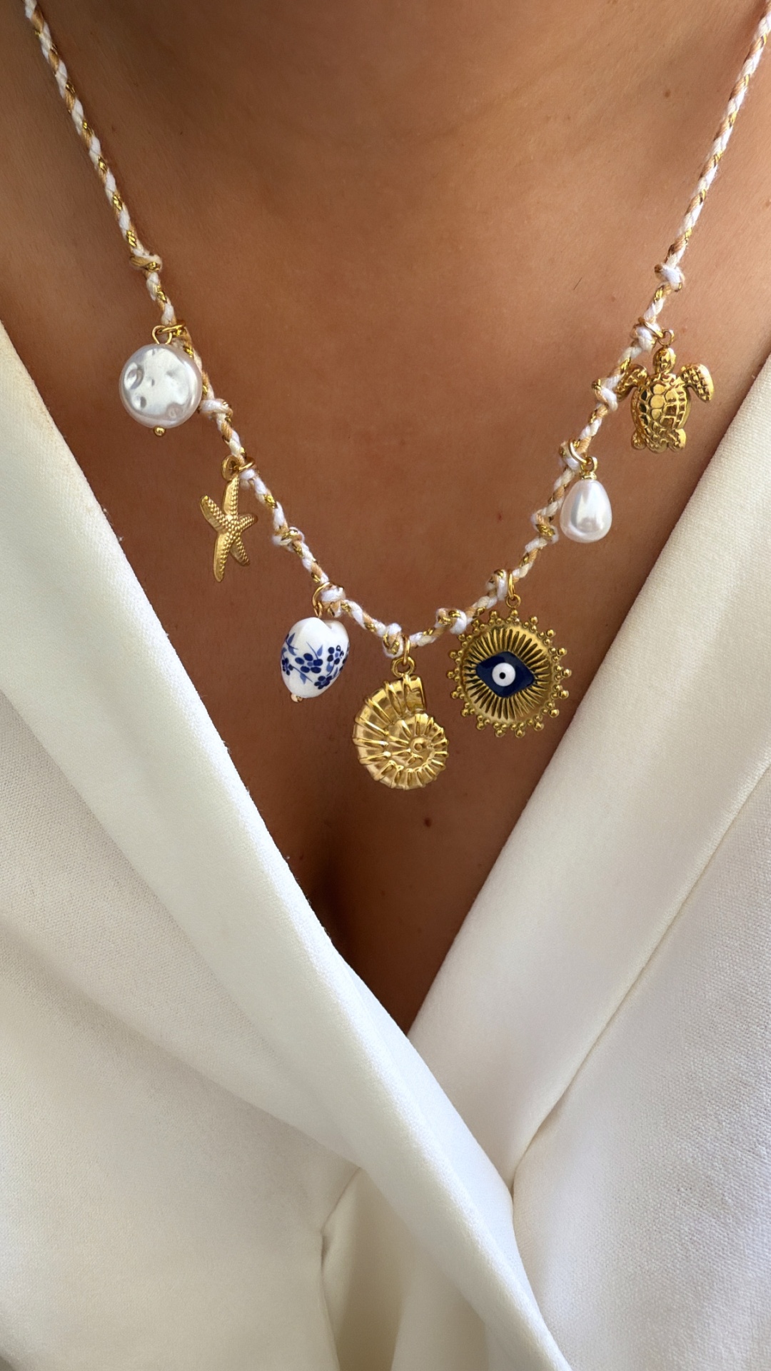 Colar com vários pendentes dourados e em branco, usado sobre uma blusa branca.