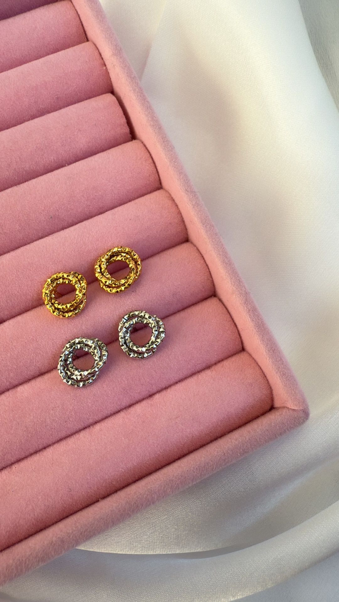 Quatro brincos circulares dourados e prateados em caixa rosa de veludo sobre tecido branco