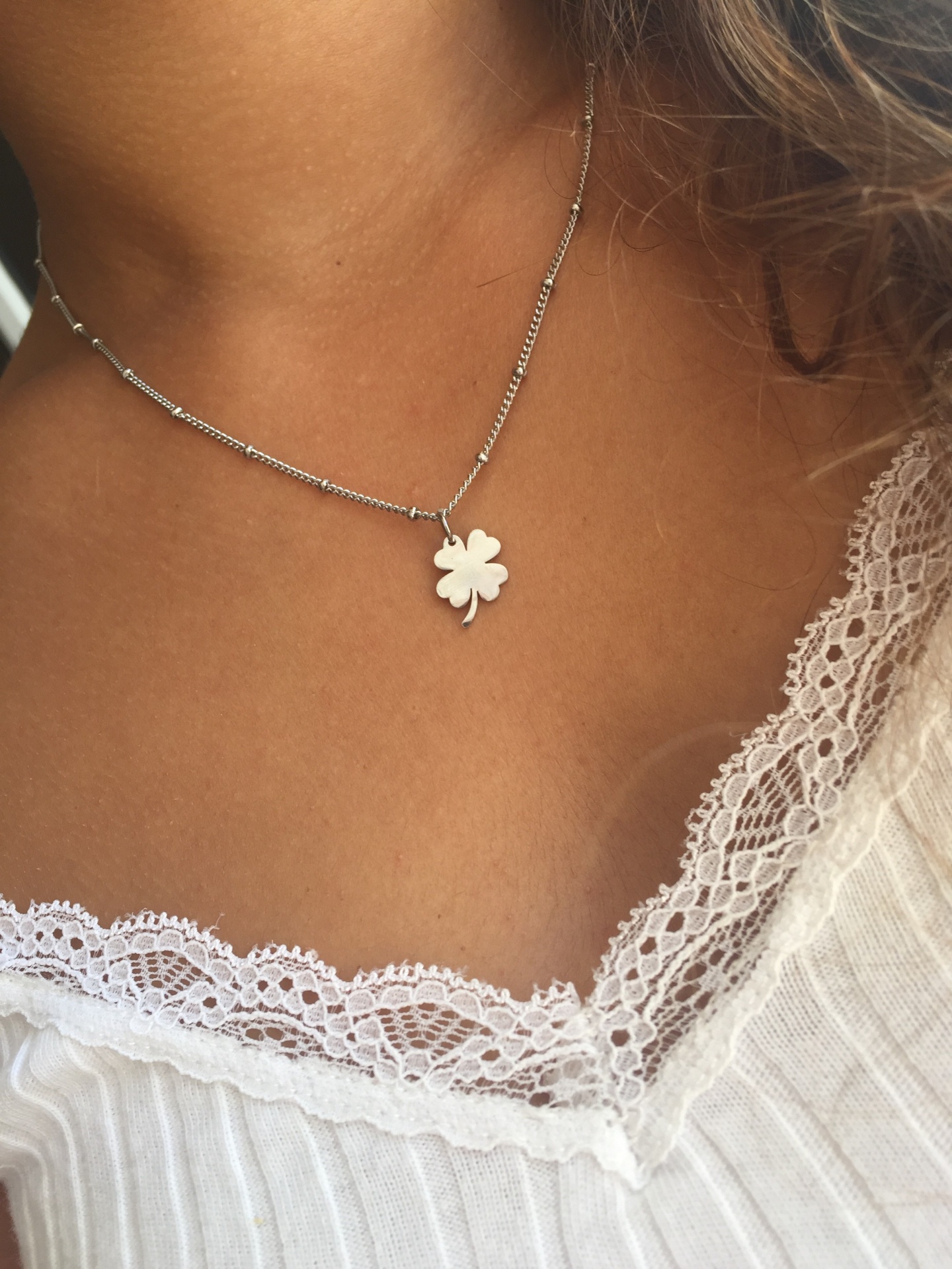 Colar prateado com pendente de trevo de quatro folhas, usado com blusa branca de renda.