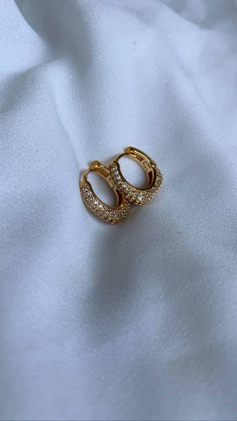 Brincos dourados em forma de argola com pedras brilhantes sobre tecido branco