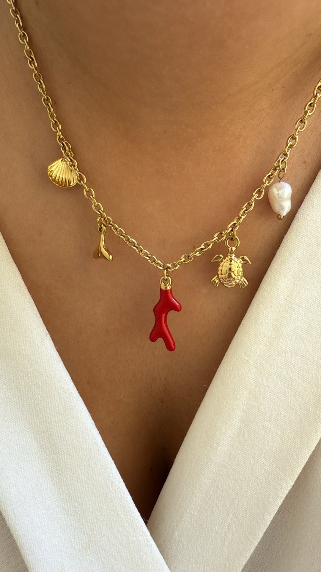 Colar dourado com pendentes marinhos e pérola sobre pele e roupa branca