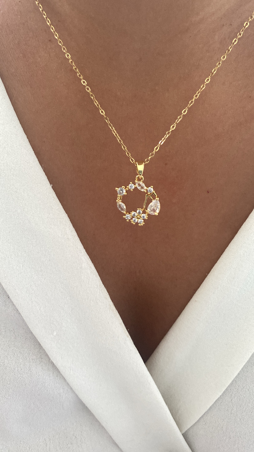 Colar dourado com pendente circular decorado com pedras, usado sobre pele e blusa branca