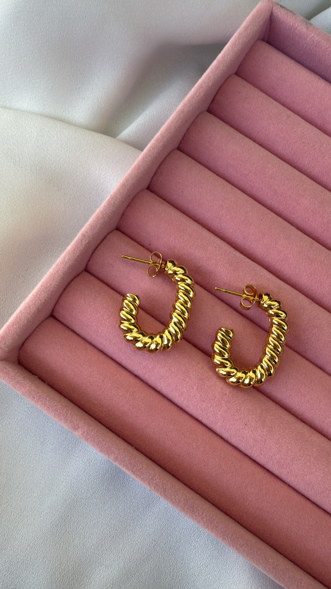 Par de brincos dourados em forma de argola com textura em espiral em caixa de veludo rosa
