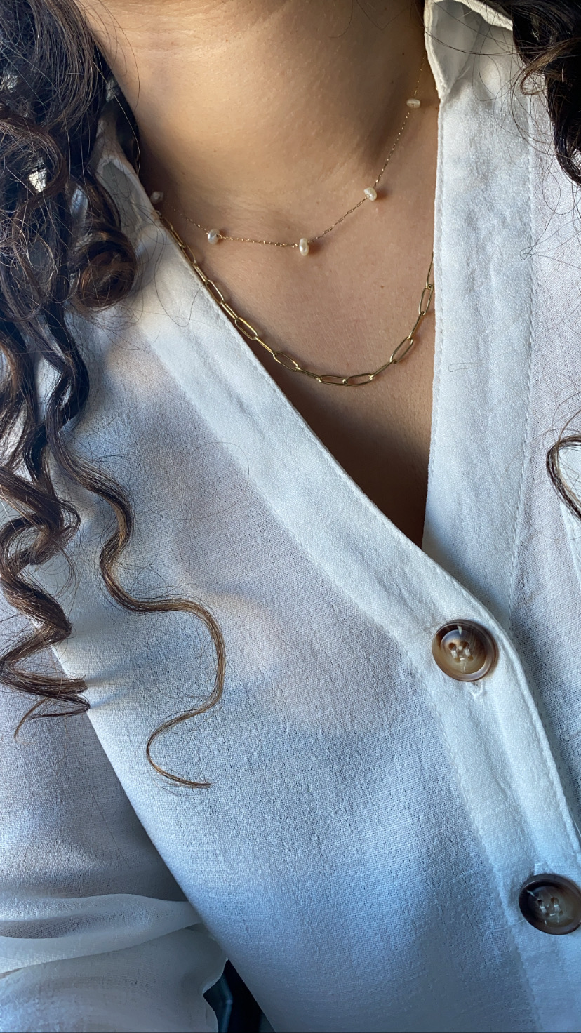 Colares dourados com pérolas e elos em pescoço com camisa branca e botões castanhos