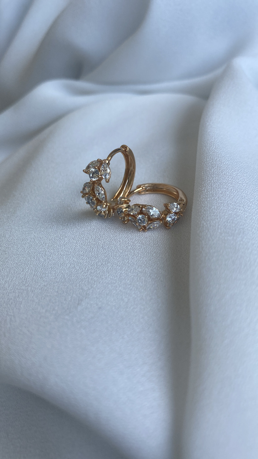 Brincos dourados com pedras transparentes sobre tecido branco