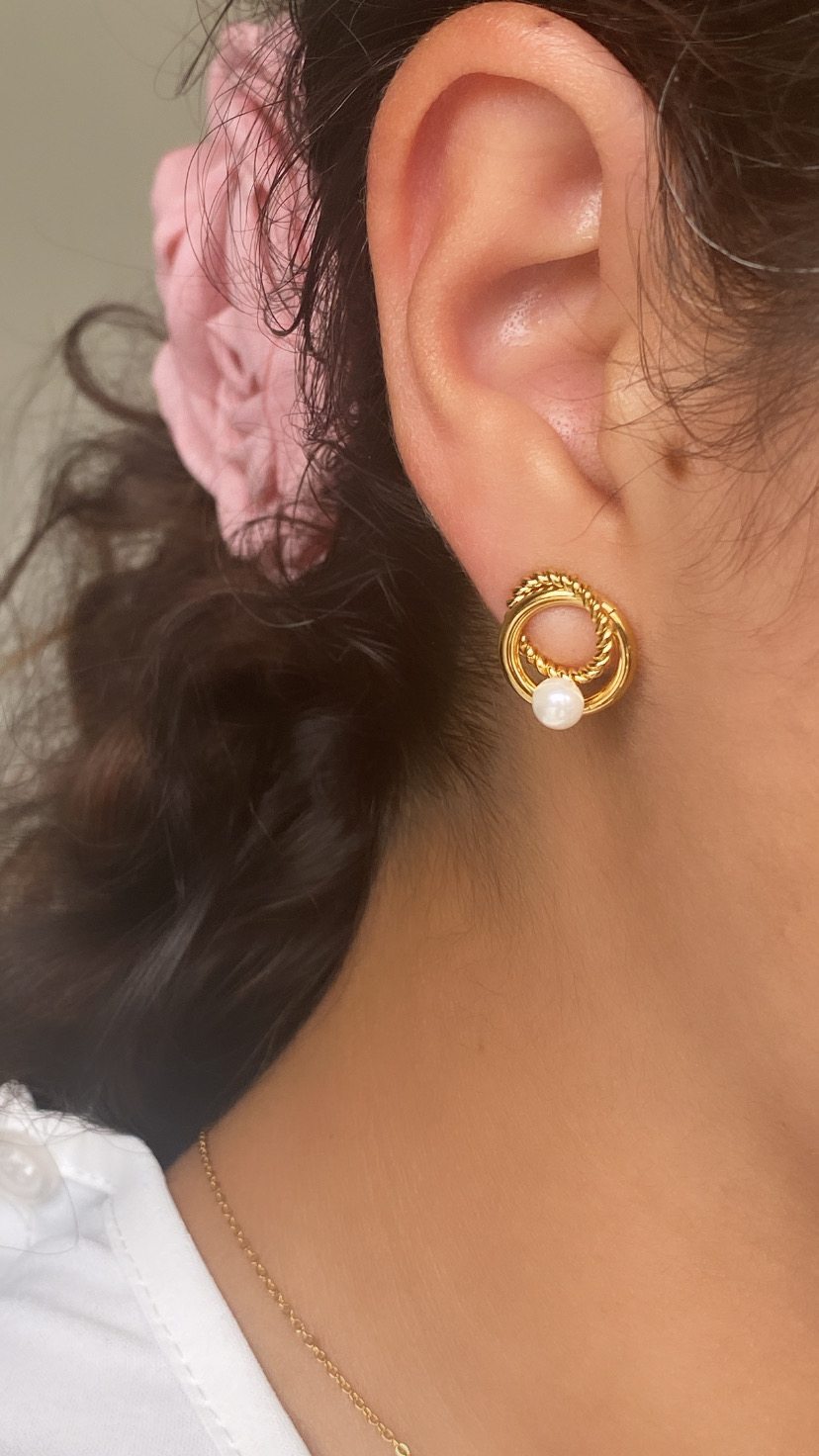 Brinco dourado circular com pérola pendurada na orelha