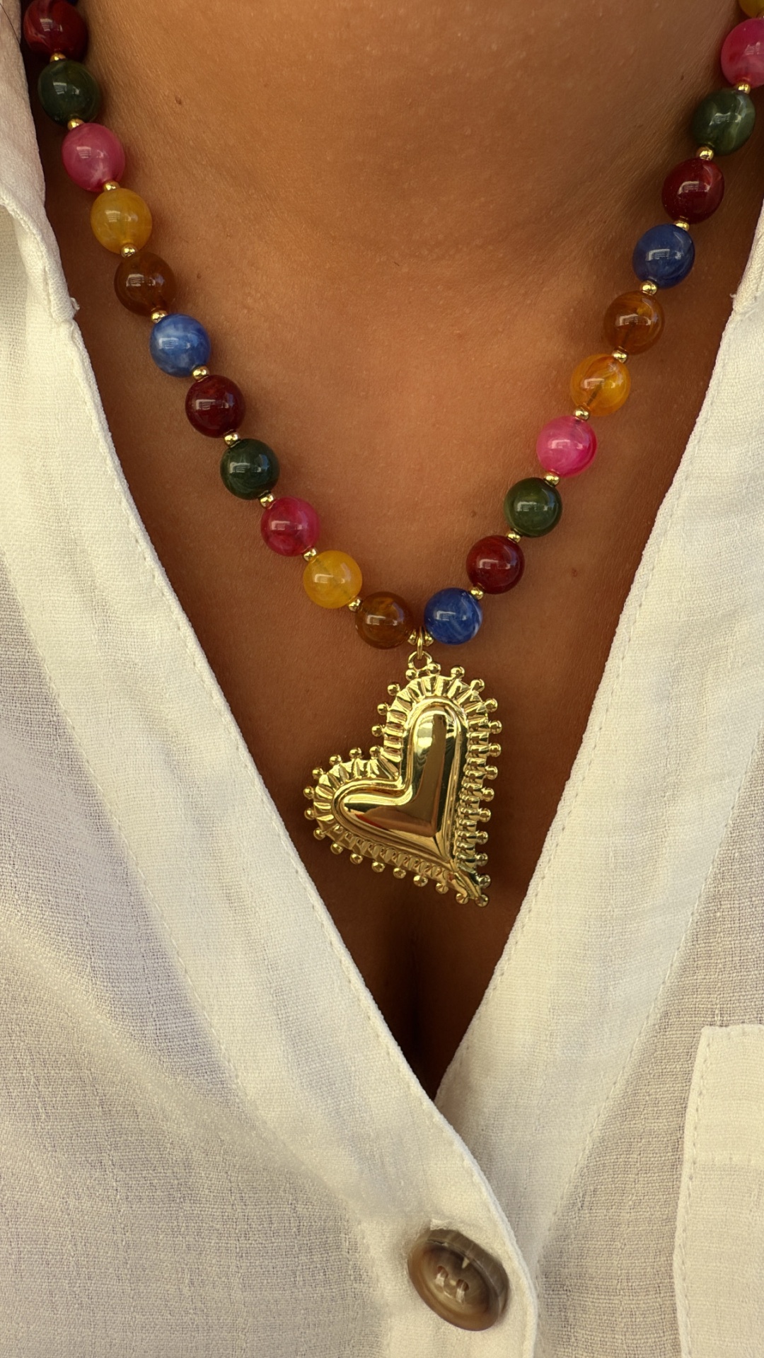 Colar colorido com pendente dourado em forma de coração sobre camisa branca