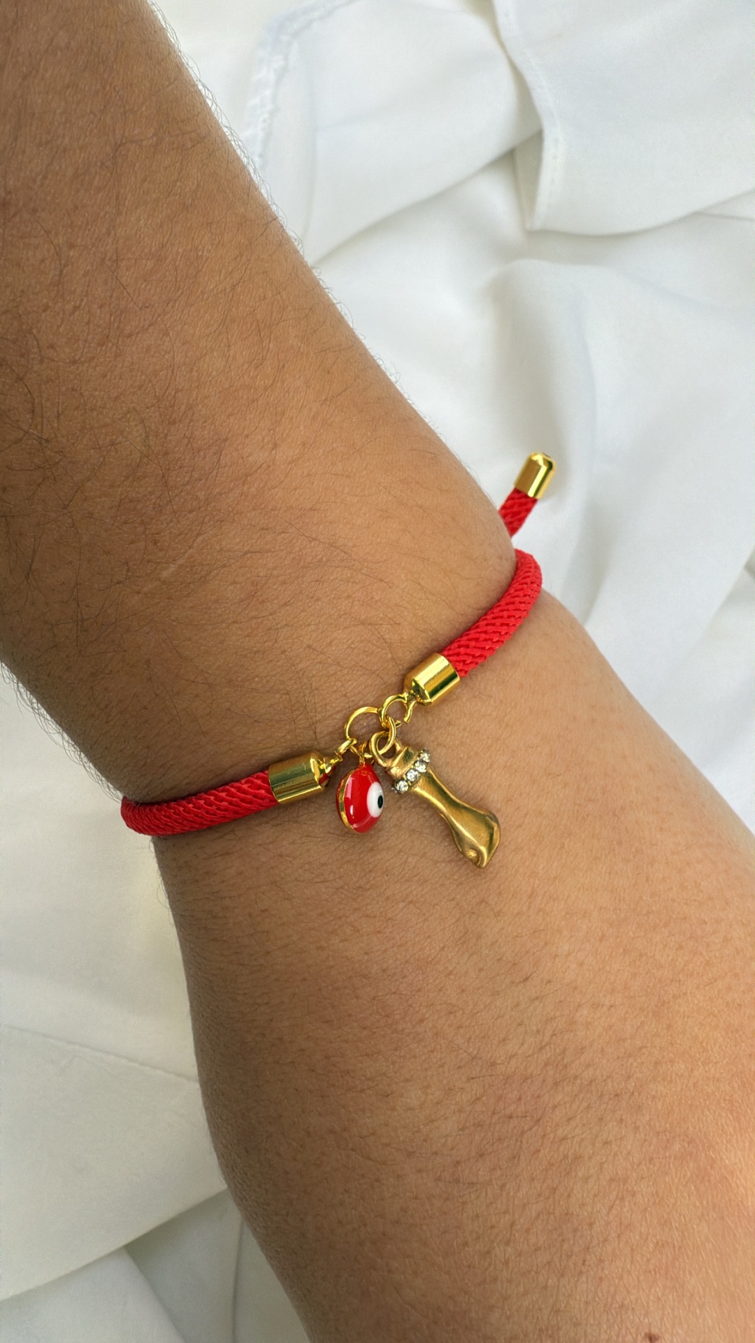 Pulseira vermelha com pingentes dourado e olho turco num pulso