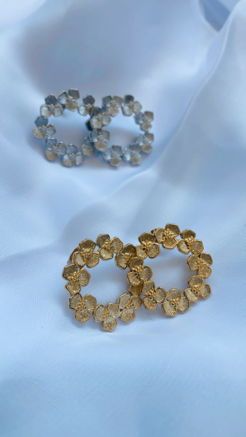 Brincos redondos de flores dourados e prateados sobre tecido branco