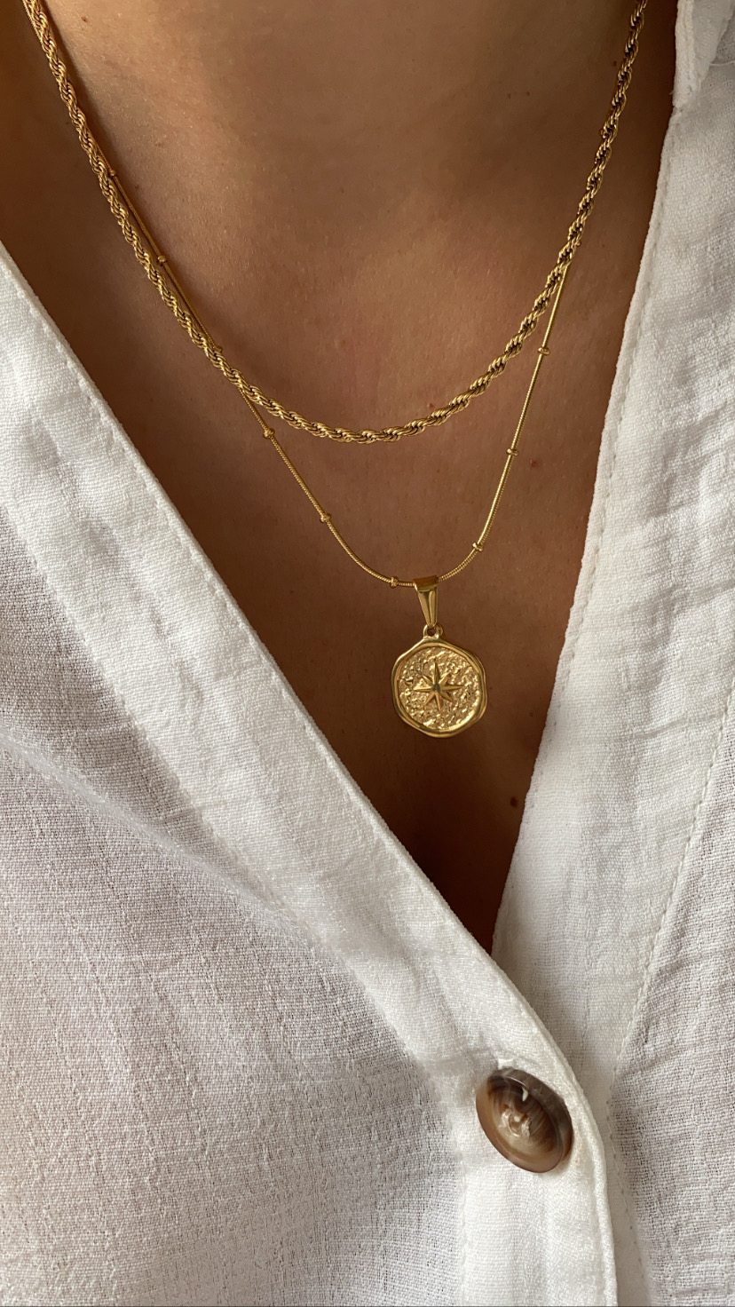 Colar duplo dourado com pendente de rosa dos ventos sobre camisa branca com botão