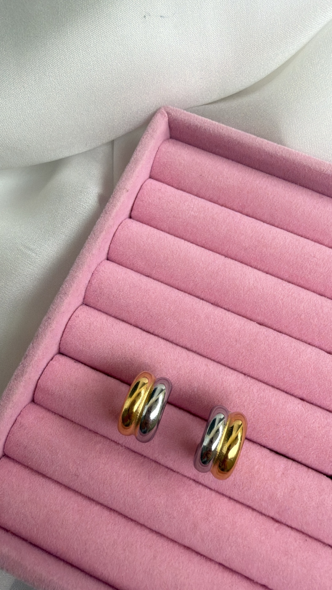 Brincos argola dupla dourado e prateado em superfície rosa acolchoada