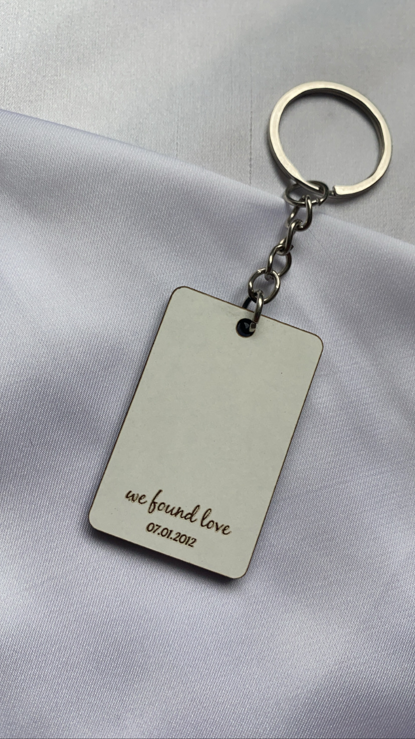 Porta-chaves metálico com pendente retangular prateado e texto gravado 'we found love 07.01.2012' sobre tecido branco
