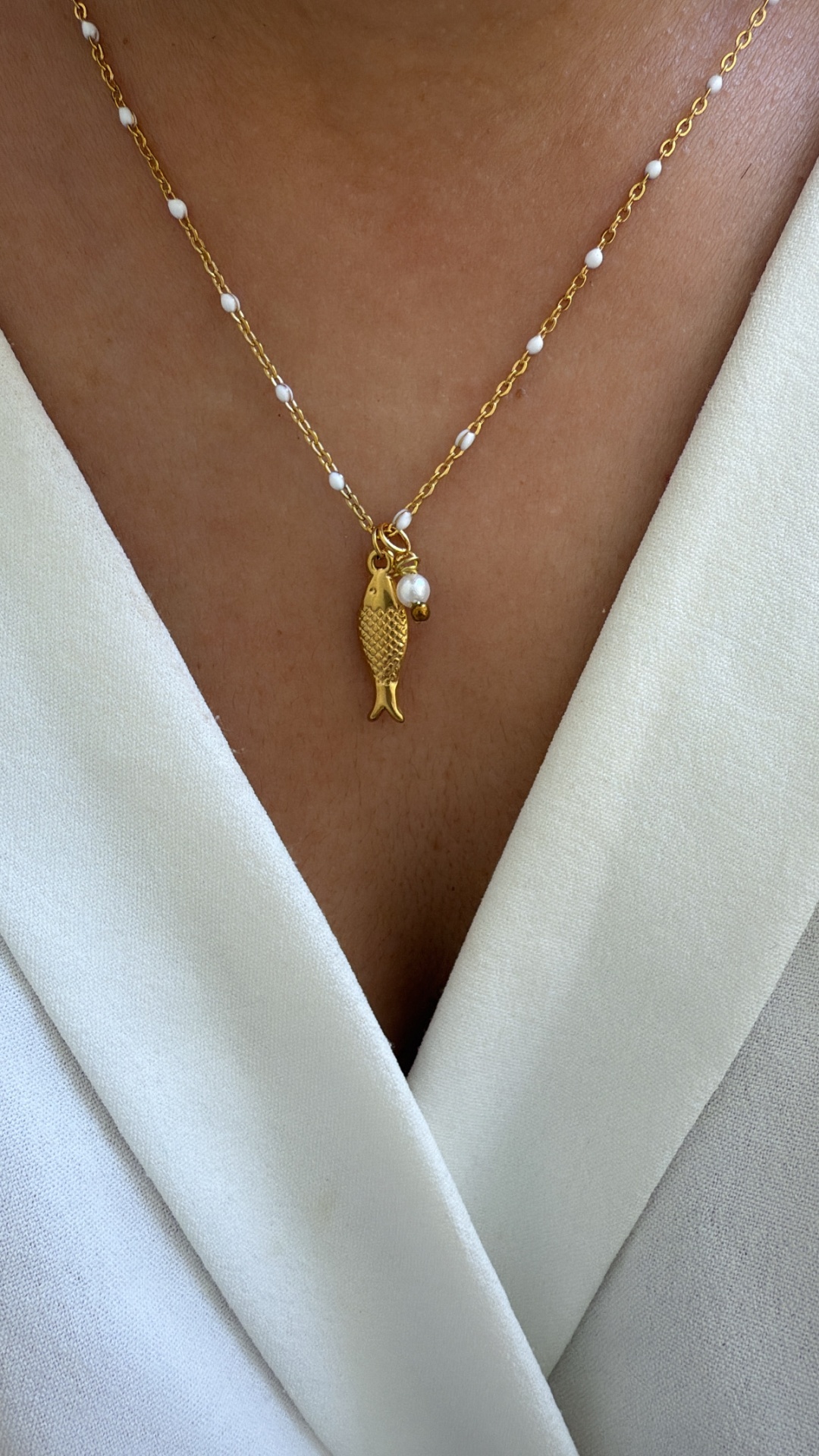 Colar dourado com pendente de peixe e pérola em roupa branca