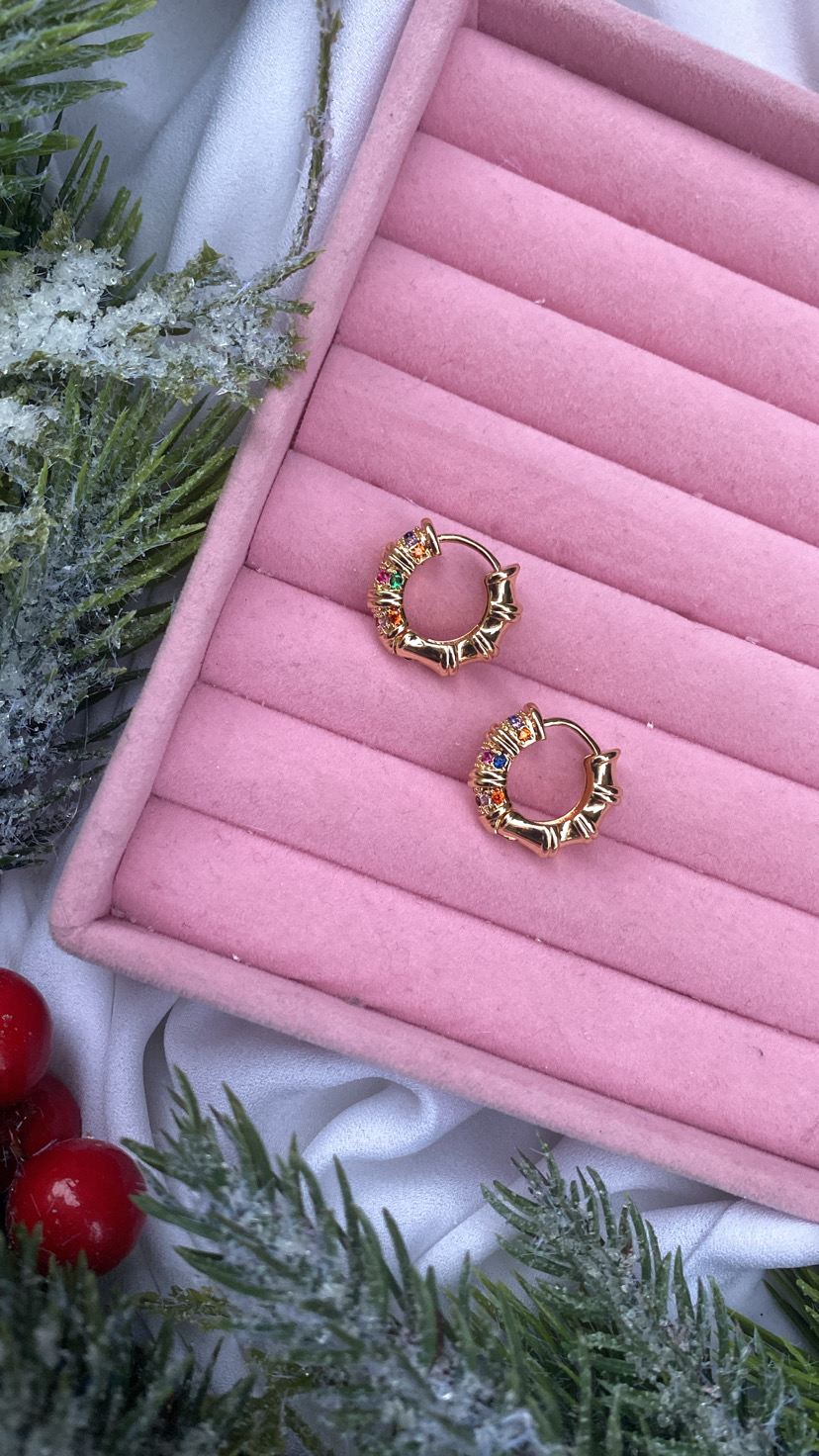 Brincos de argola dourados com pedras coloridas numa caixa rosa e decoração natalícia.