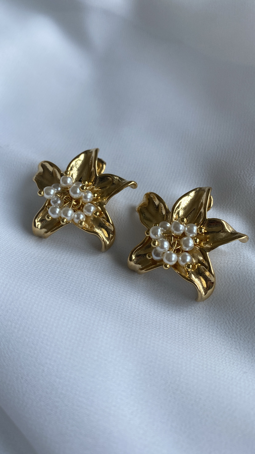 Brincos dourados em forma de flor com pérolas no centro sobre tecido branco