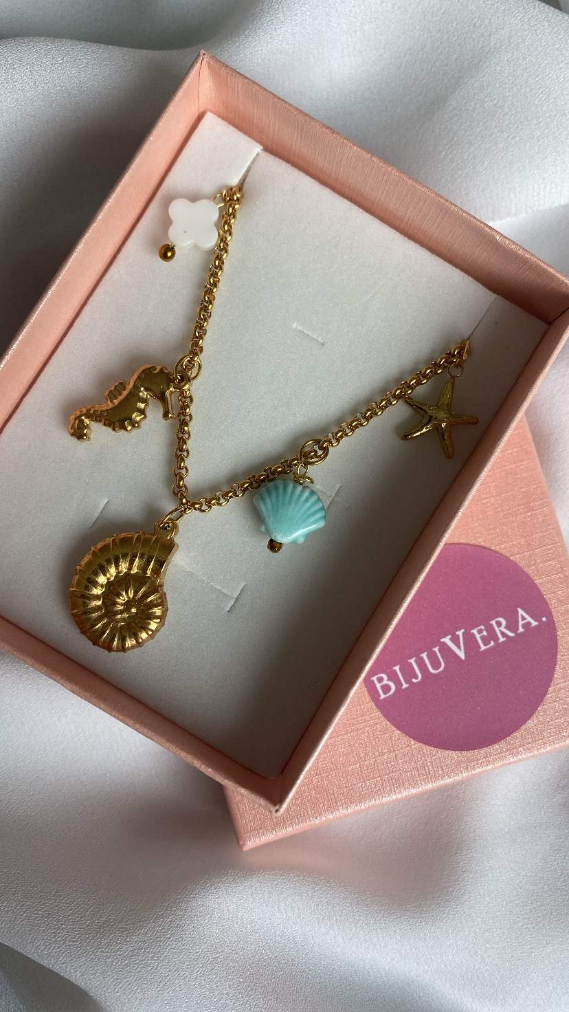 Colar dourado com pendentes marinhos numa caixa de joias rosa e etiqueta BIJUVERA
