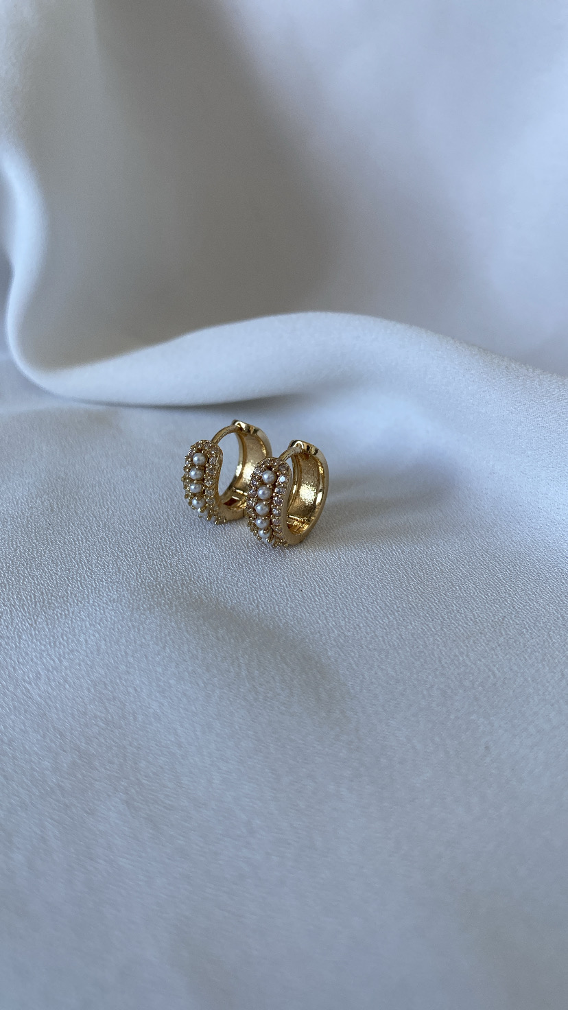 Brincos de argola dourados com pérolas sobre tecido branco