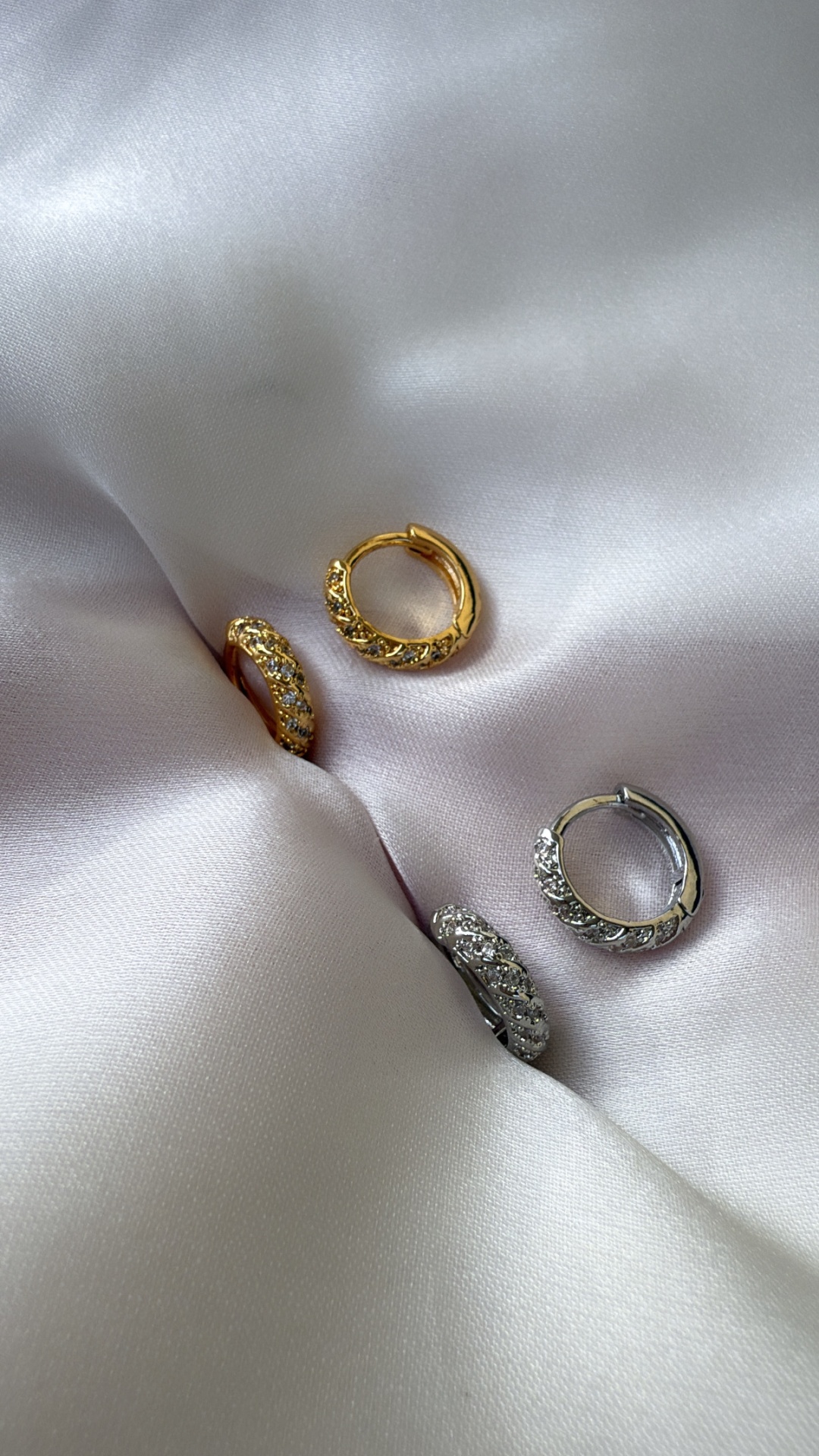 Brincos argola dourados e prateados com pedras sobre tecido branco acetinado