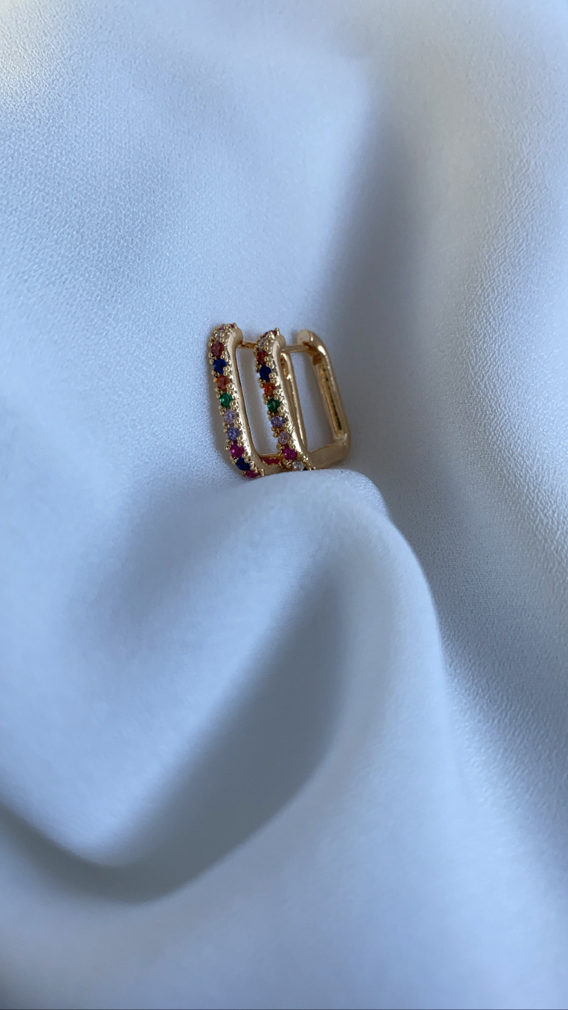 Brincos dourados com brilhantes coloridos sobre tecido branco